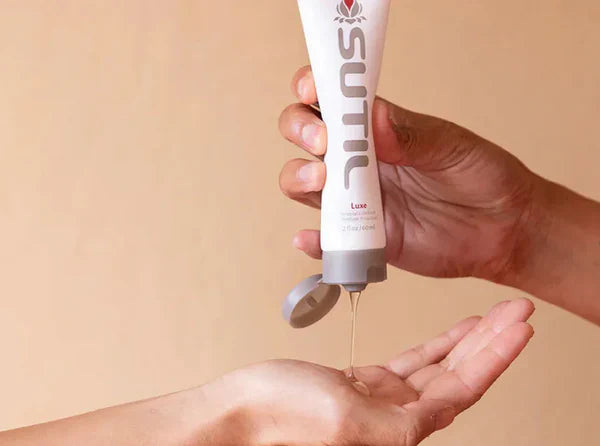 Close-up of a hand dispensing a drop of body-safe personal lubricant into an open palm